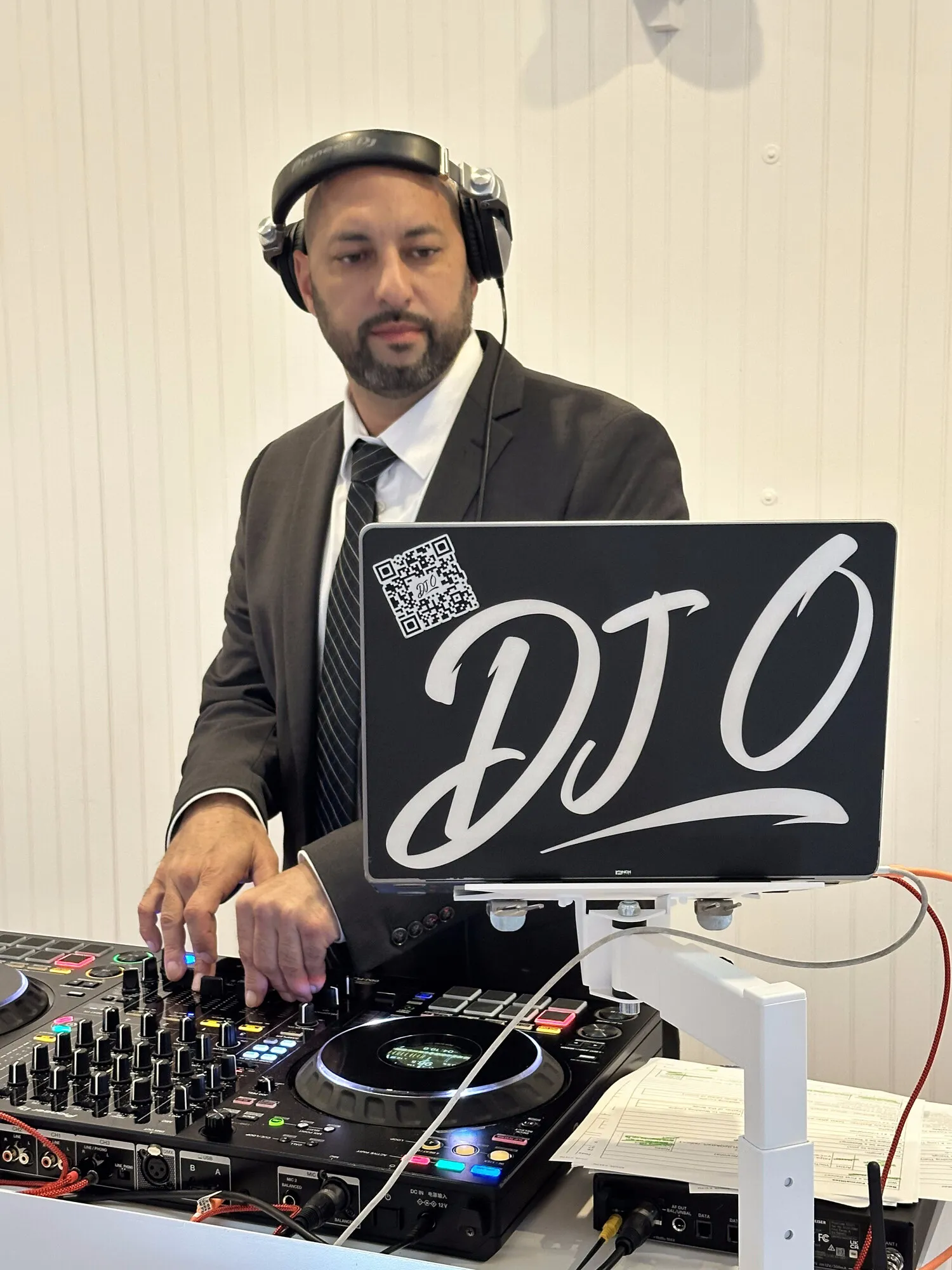 DJ O in a suit and headphones, mixing at a reception